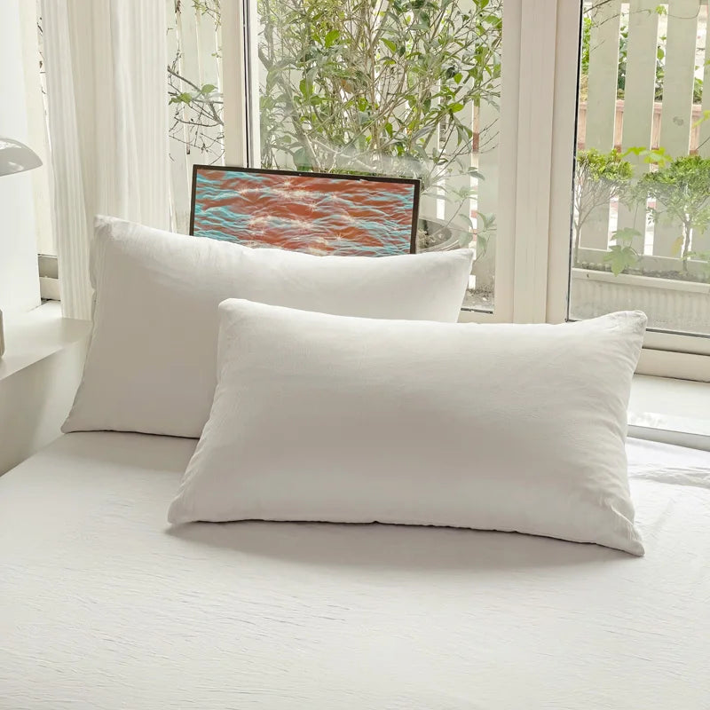 Set of two ultra-soft cotton-blend pillowcases in a minimalist solid colour, styled on a neutral-toned bed for a relaxed, cosy look.