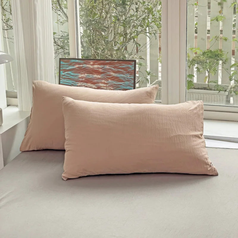Set of two ultra-soft cotton-blend pillowcases in a minimalist solid colour, styled on a neutral-toned bed for a relaxed, cosy look.