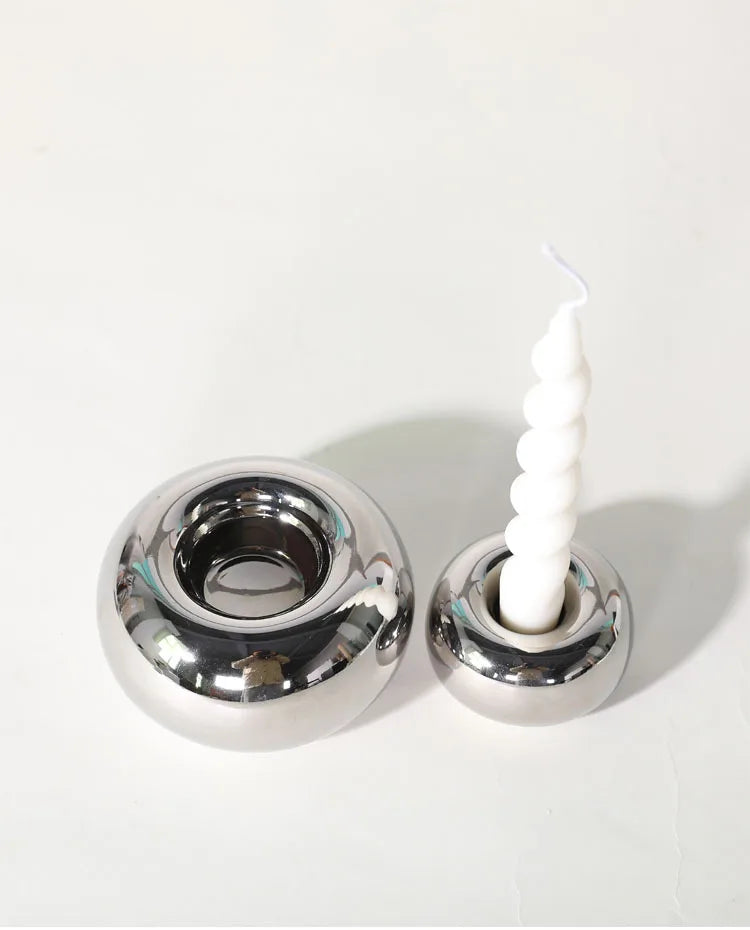 Modern silver ceramic candle holder with a sleek cylindrical design, shown in two sizes on a neutral-toned surface.