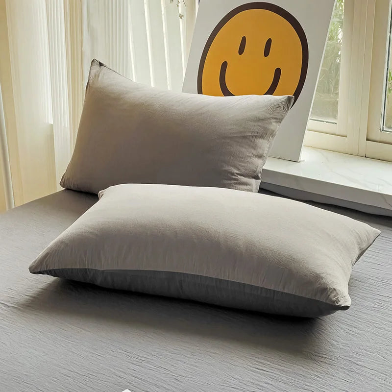 Set of two ultra-soft cotton-blend pillowcases in a minimalist solid colour, styled on a neutral-toned bed for a relaxed, cosy look.
