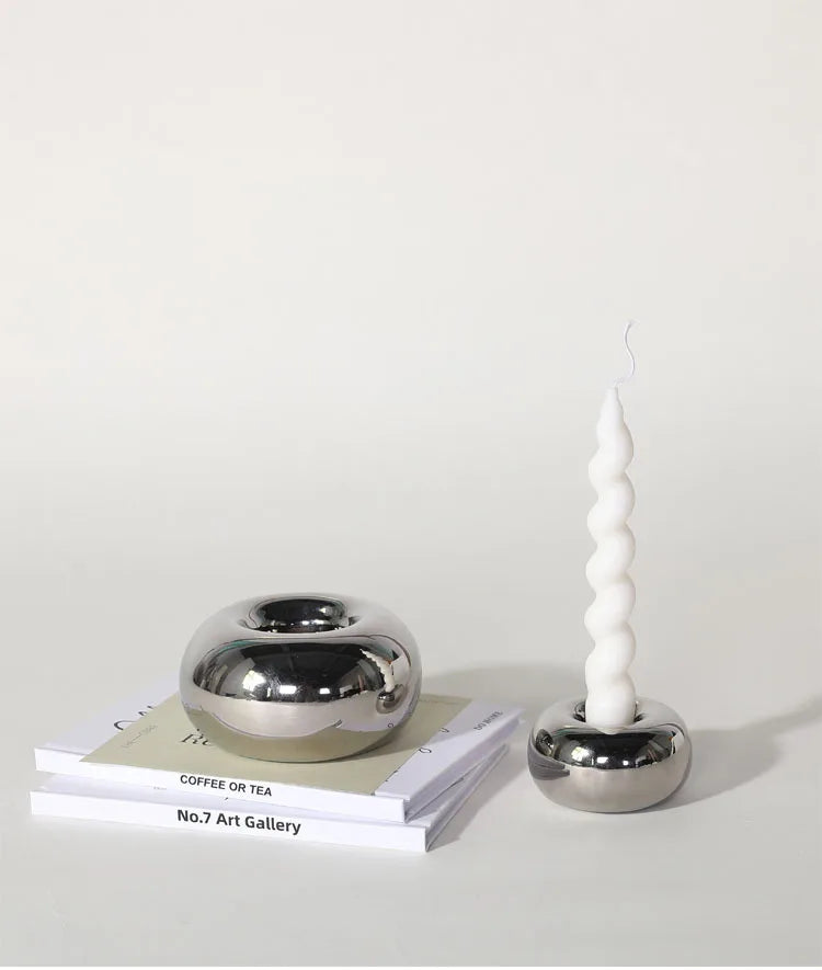 Modern silver ceramic candle holder with a sleek cylindrical design, shown in two sizes on a neutral-toned surface.