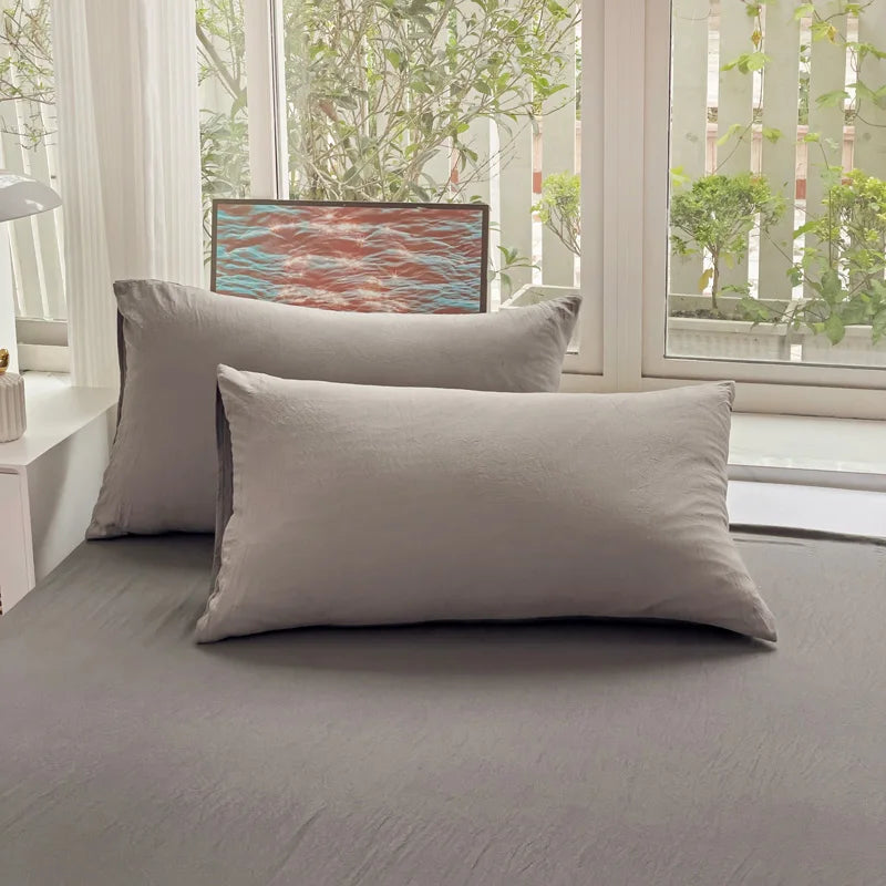 Set of two ultra-soft cotton-blend pillowcases in a minimalist solid colour, styled on a neutral-toned bed for a relaxed, cosy look.